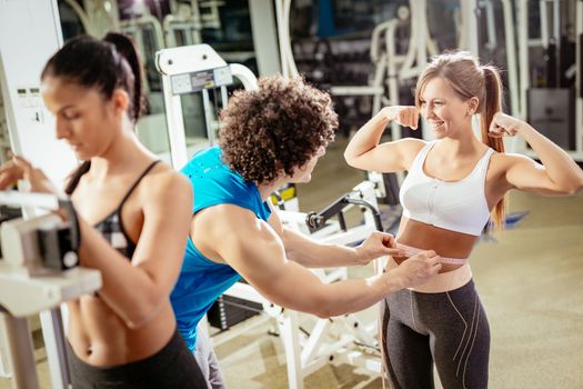 Fitness instructor measuring woman's waist in gym.