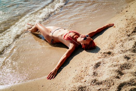 Beautiful young woman enjoying on the beach. She is lounging and sunbathing on the sandy coast in the sea. 