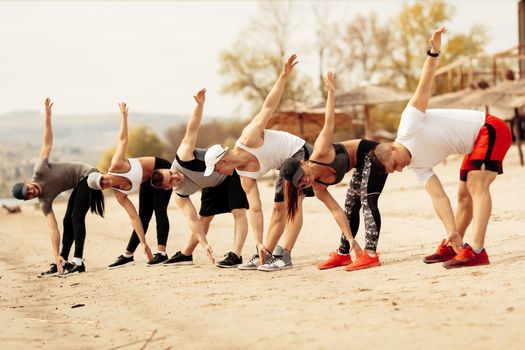 Group happiness young friends having workout together on the beach. They are doing warming exercise.