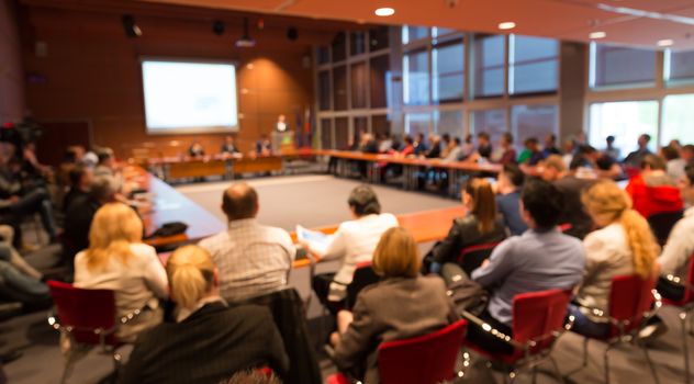 Speaker giving a talk on corporate business event. Audience at the conference hall. Business and Entrepreneurship event. Focus on unrecognizable business people in the rear.