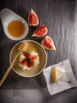 A wheel of melted brie covered in sliced figs and honey  on a stone plate.