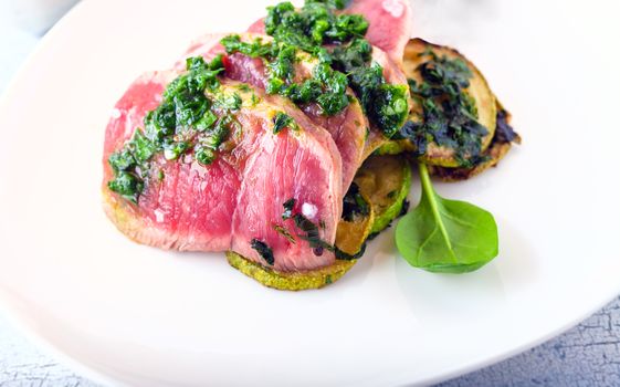 A plate of sliced roast beef, zucchini and salsa verde