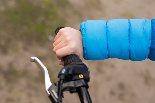 A boy in a blue jacket holds a bicycle handlebars.