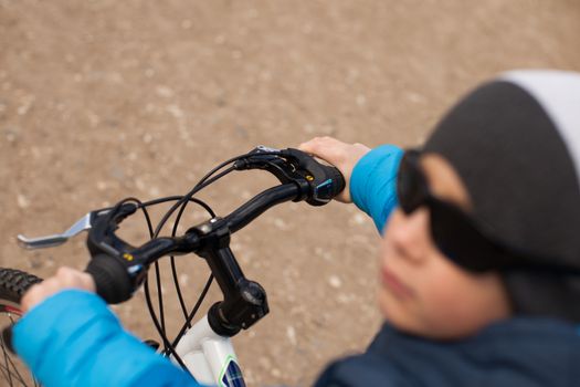A boy in a blue jacket holds a bicycle handlebars.