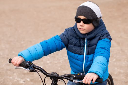 A boy in a blue jacket holds a bicycle handlebars.