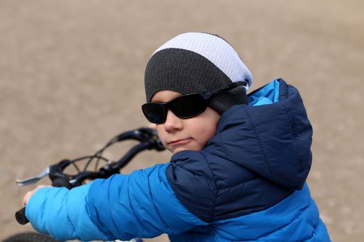A boy in a blue jacket holds a bicycle handlebars.