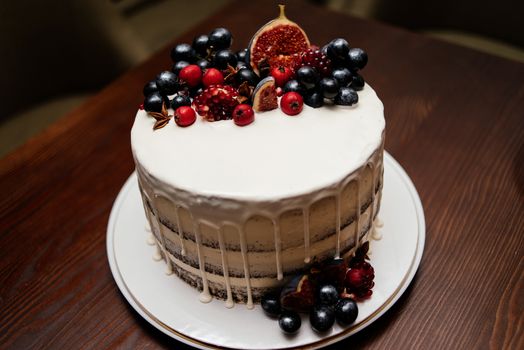 Birthday cake decorated with fresh fruits on the white plate on a wooden table. Wedding cake with fruits