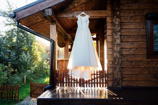 A beautiful cream wedding dress hanging on the wall near the wooden house