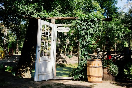 Wedding arch with white door overgrown with ivy and decorated with flowers  in jars and lights. Wedding rustic photozone