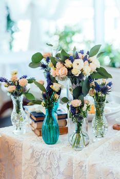 Сream and blue flowers in vases on a table with a lace tablecloth. Wedding decorations