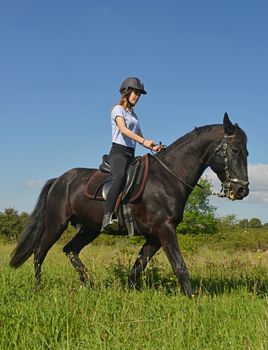 young riding girl and her black stallion in nature