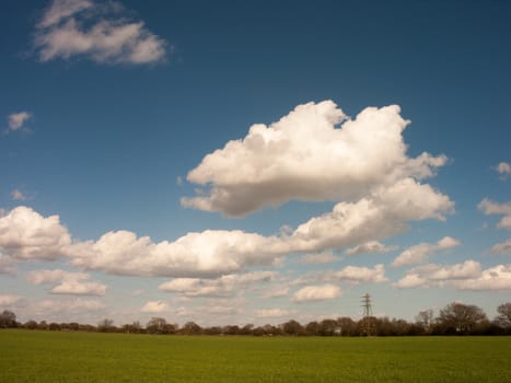 Some white crips clouds hanging over a field on a sunny day