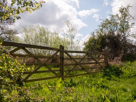 A Glorious and Stunning Wooden Gate and Fence in the Countryside Closing off a Farm Field with Lush Grass and Plants around it and trees, beautiful blue stunning sky and fresh grass, wooden and locked