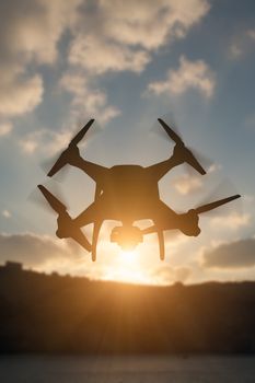 Silhouette of Unmanned Aircraft System (UAV) Quadcopter Drone In The Air At Sunrise.