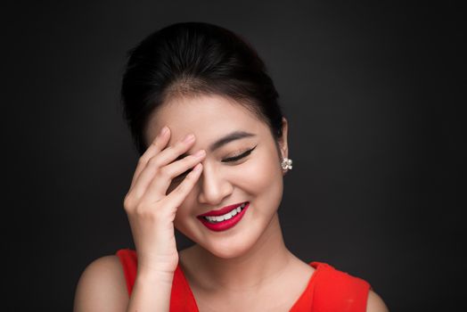 Smiling shy woman closed her face with a hand over black background.