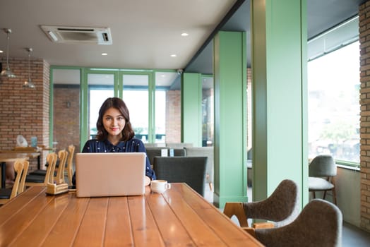 Beautiful cute asian young businesswoman in the cafe, using laptop and drinking coffee smiling