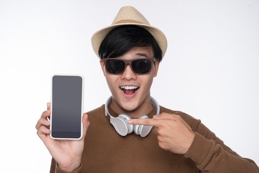 Smart casual asian man seated on chair, showing smartphone screen in studio background
