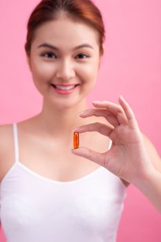 Young asian beauty young woman eating pills and drinking water on pink background.