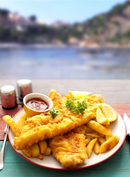 Two pieces of battered fish on a plate with chips by the coast 