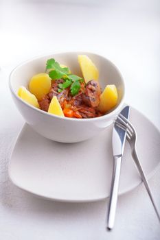 Beef stew being in a slow cooker, garnished with potatoes and champignons