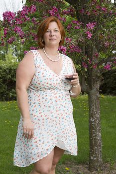 forty something woman wearing a summer dress, having a glass of red wine under a cherry tree