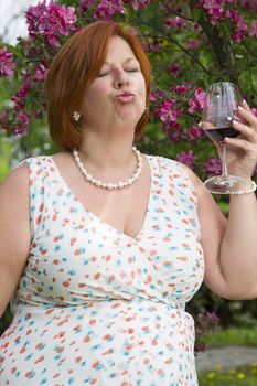 forty something woman wearing a summer dress, tasting a red wine under a cherry tree