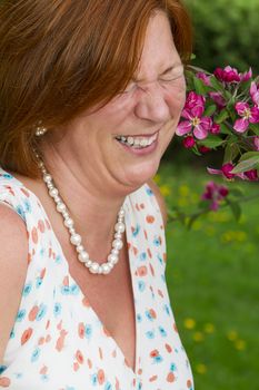 Woman in her forties wearing a summer dress, laughing near flowers