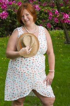 forty something woman wearing a summer dress, holding a hat to her chest