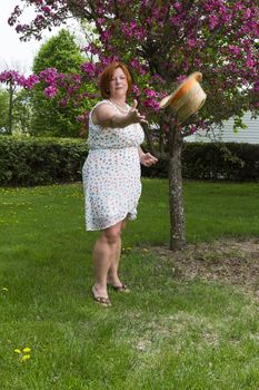 forty something woman wearing a summer dress, throwing a straw hat