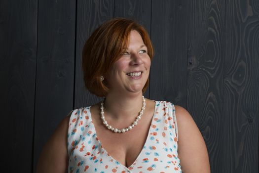 forty something overweight woman wearing a summer dress in front of a blue wood stain background