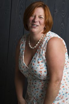 forty something overweight woman wearing a summer dress in front of a blue wood stain background