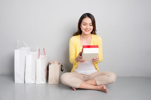 Young asian woman sitting besides row of shopping bags holding red gift box