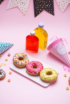 Party. Different colourful sugary round glazed donuts and bottles of drinks on pink background.
