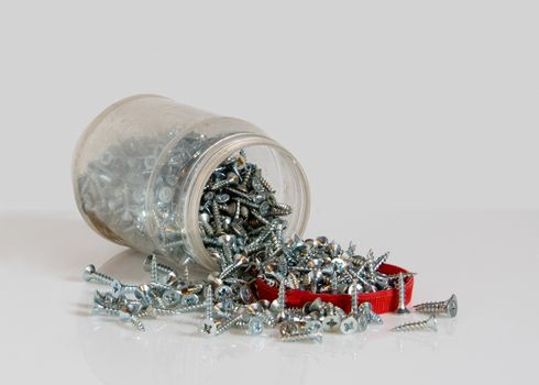 Transparent can with a red lid and scattered screws. Photo on the white background