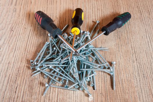 Three different screwdrivers lie on a pile of screws