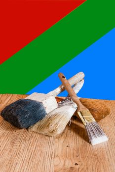 Old big paint brushes lie on a wooden board against a colored background
