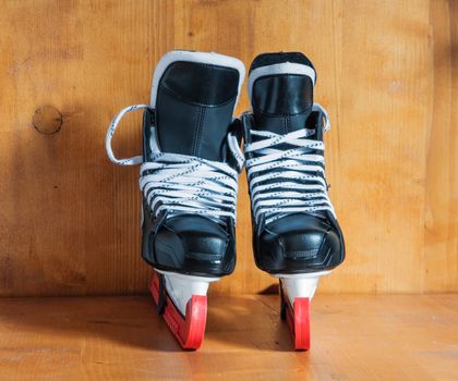 Professional hockey skates with red protective covers, against the wooden background

