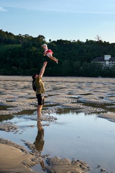 Father throws his daugter at the beach near the sea with the forest and the sky in the background. Reflection in the water
