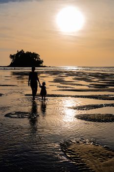 Mother with daughter going to the beautiful colorful sunset near the smal eaxotic island with palms