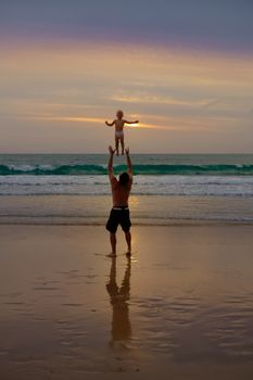 Father throws his daugter at the beach near the sea at the spectacular cloudy sunset