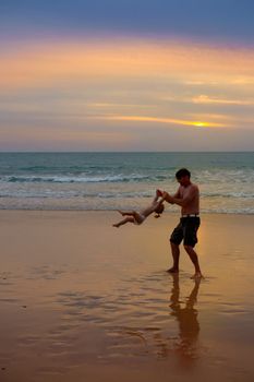 Father plays with his daugter at the beach near the sea at the spectacular cloudy sunset