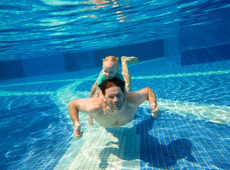 Father dives with young daughter in the pool. Little girl rides daddy's back underwater