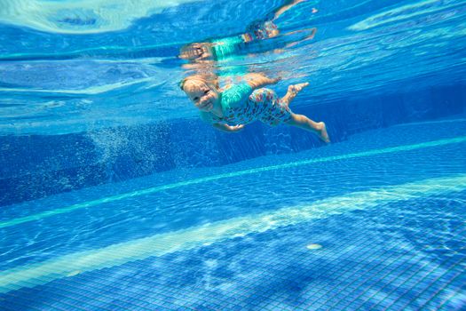 Little girl diving underwater in the pool and smiling