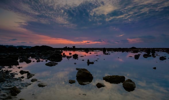 Colourful sunrise, stones and reflections in low tide ocean water