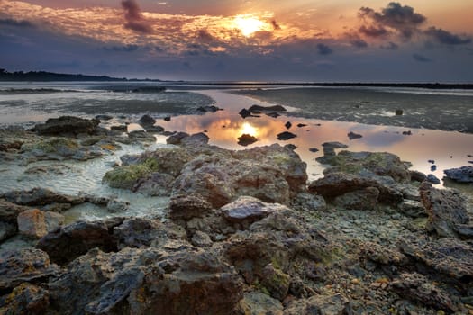 Colourful sunrise and stones in  low tide ocean water