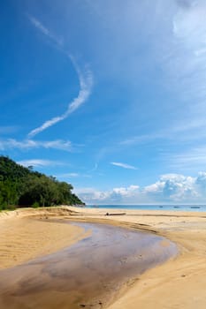 Small river flows into the sea in sunny day with just some clouds on tropical island