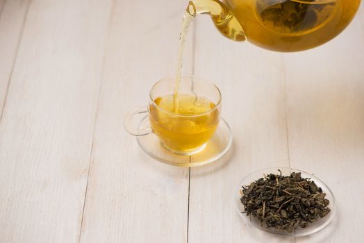 Pouring tea. Cup of hot tea and tea leaf on the wooden table