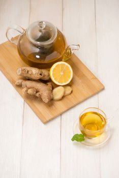 Cup of ginger tea with lemon and honey on white wooden background.