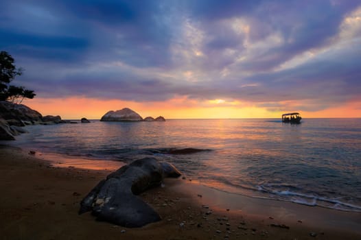 Colorful cloudy sunset at tropical exotic island. Boat, stones, rocks, sand, water, clouds, sun.