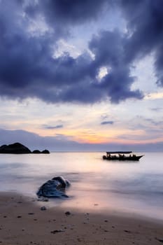 Long exposure. Boat in the sea at pictureous cloudy sunset. Sand and stone. Rocks in the sea.